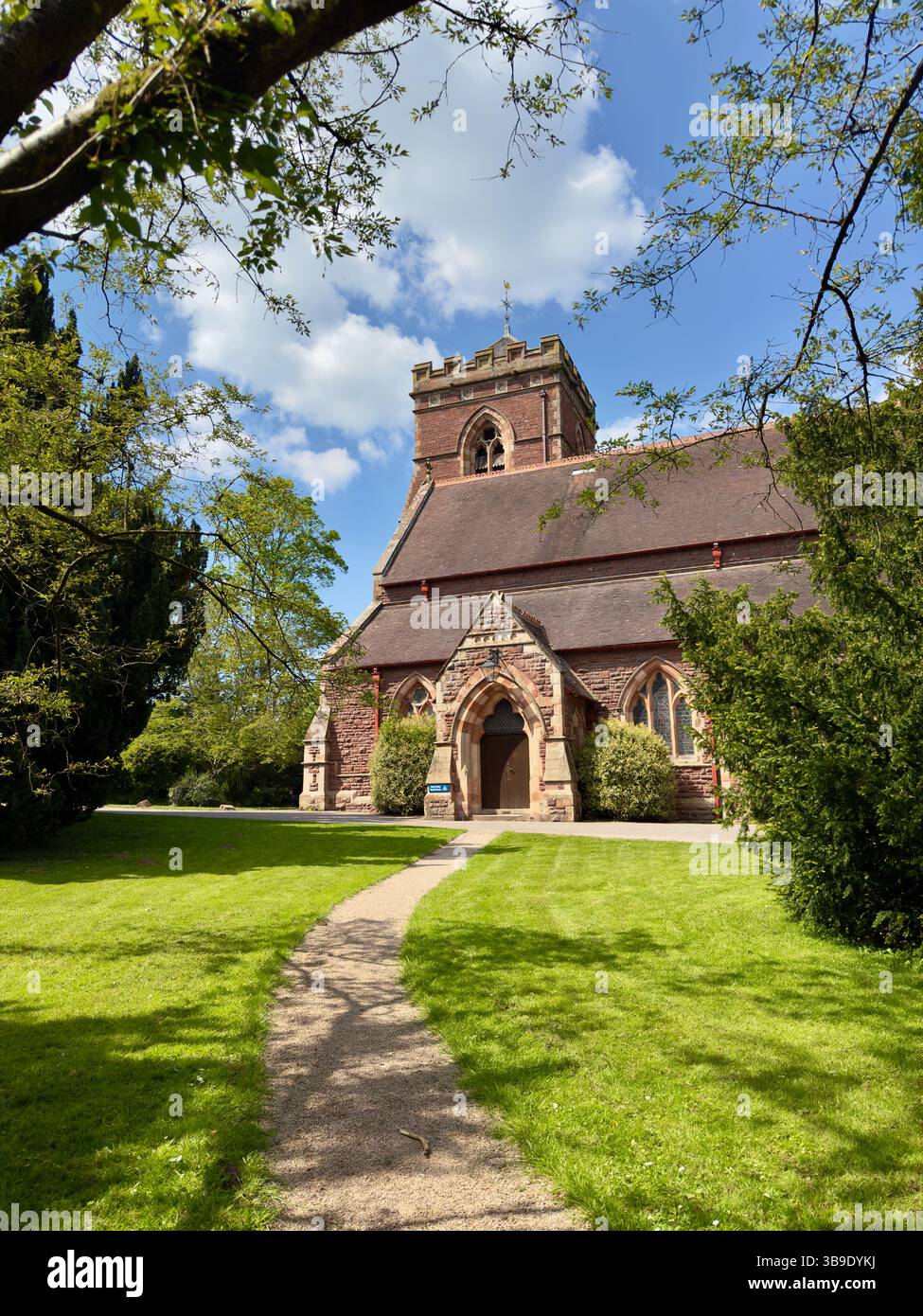 Sandsteinkirche umgeben von Bäumen an einem sonnigen Frühlingstag. Heilige Dreifaltigkeit Meole Brace, Shrewsbury in einem gepflegten Kirchhof. - Smartphone-aufgenommenes Stockfoto