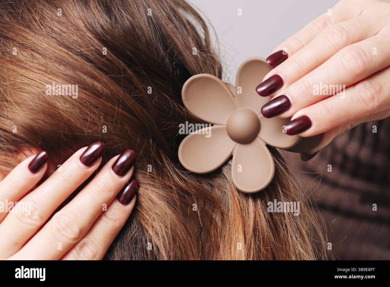 Frau, die Haare mit großem Blumenklemme stylt. Braune Kunststoffspange in Form einer Blume. Großaufnahme der Hände und Frisur. Haarschmuck und Schönheit. Stockfoto