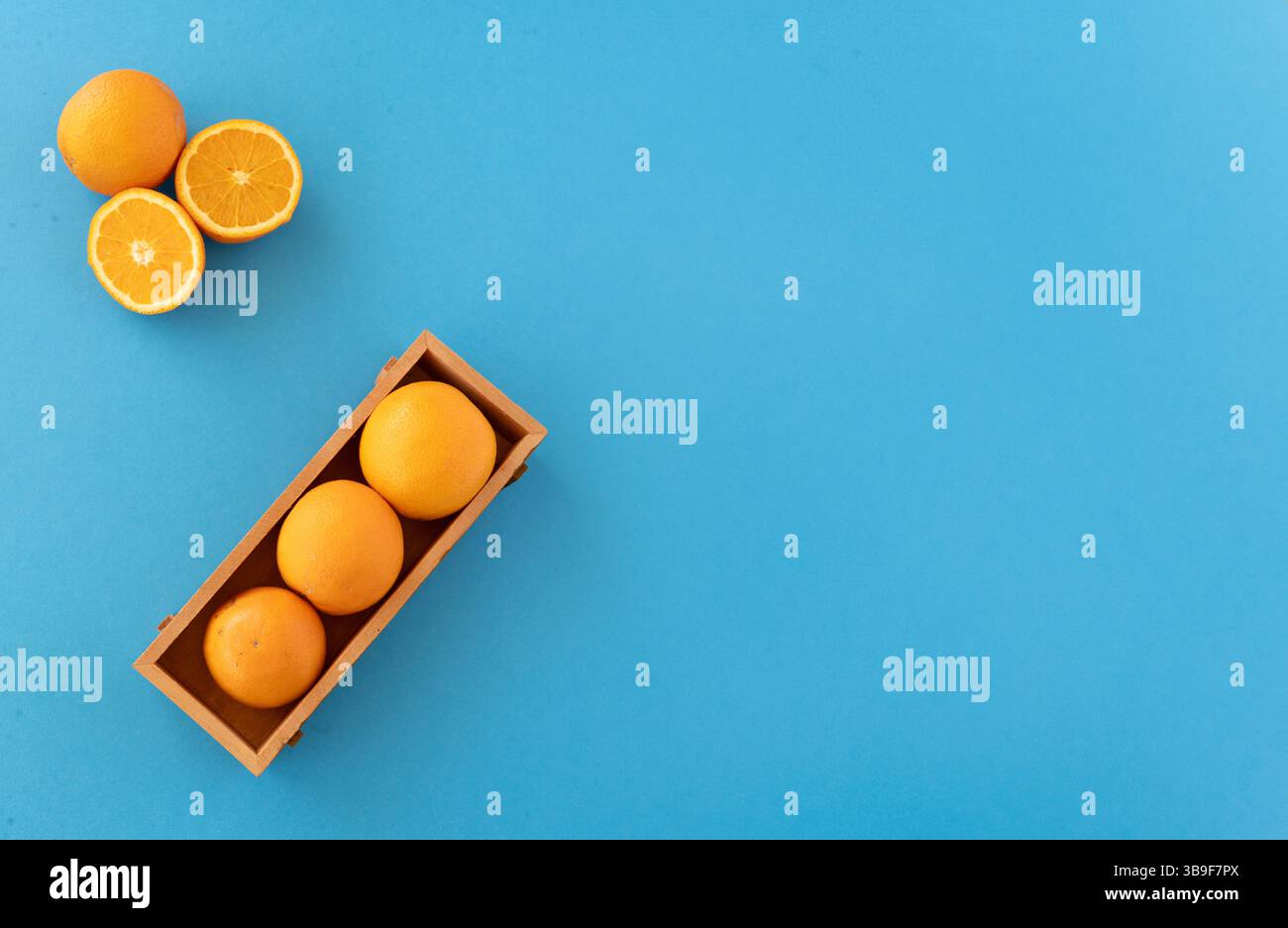 Drei Orangen in einer Holzkiste und frische geschnittene Zitrusfrüchte auf blauem Hintergrund helle natürliche Töne heben Frische und gesunden Lebensstil hervor.natürliches Holz Stockfoto