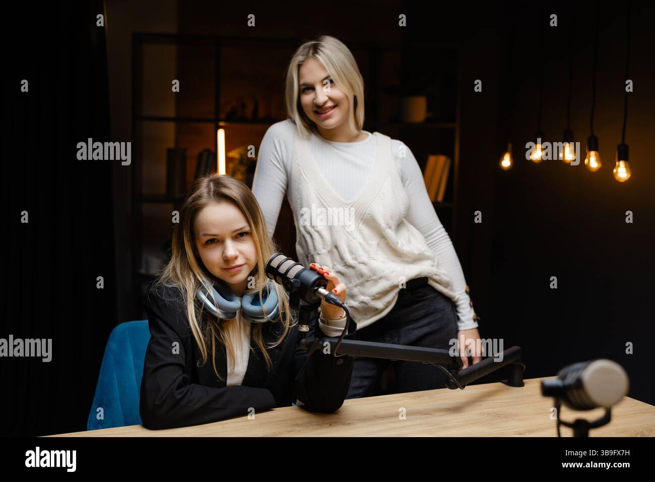 Zwei weibliche Podcasterinnen, die während der Live-Aufnahme in einem professionellen Studio eine gute Geste machen und Selbstvertrauen und Positivität ausstrahlen Stockfoto