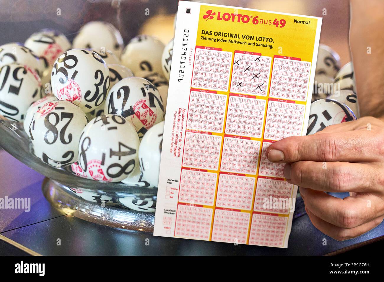 Bayern, Deutschland - 9. Mai 2025: FOTOMONTAGE, Ein abgeschlossenes Lotterieticket wird neben einer Schüssel voller Draw Balls abgehalten - der Moment vor der Lotterieverlosung, der Hoffnung auf Glück und großen Sieg weckt. *** FOTOMONTAGE, ein ausgefüllter Lottoschein wird neben einer Schale voller Ziehungsbälle halten der Moment vor der Lottoziehung, der Hoffnung auf Glück und einen großen Gewinn weckt. Stockfoto