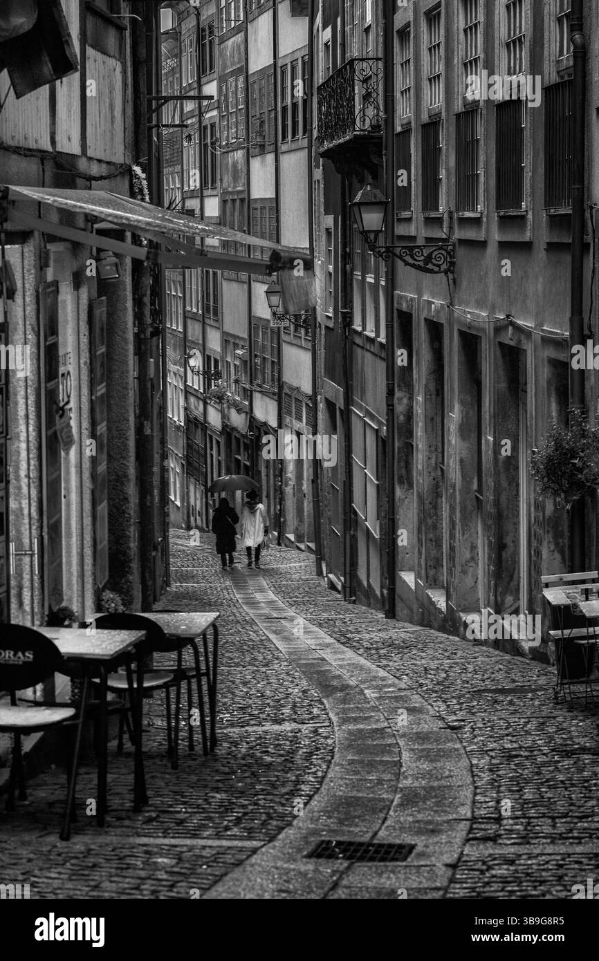 Leute mit Sonnenschirmen laufen durch eine Straße in der Altstadt von Porto&#39. Tische und Stühle stehen im Vordergrund, Portugal Stockfoto