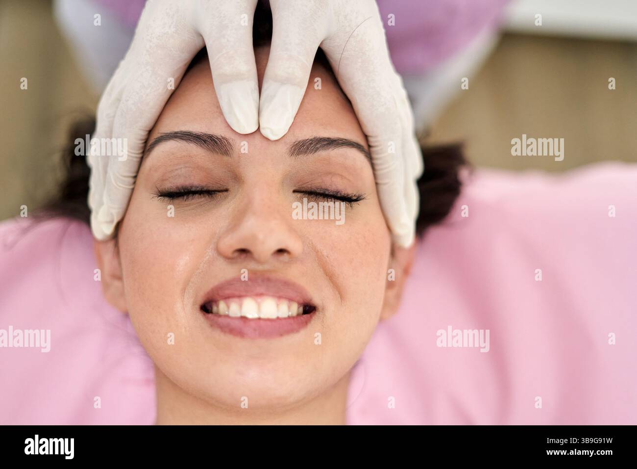 Ein Kunde genießt eine wohltuende Gesichtsmassage in einem Schönheitssalon, der auf ästhetische Medizin spezialisiert ist. Der Therapeut setzt schonende Techniken ein, um relaxa zu fördern Stockfoto