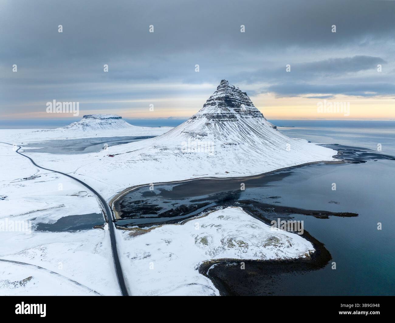 Ein atemberaubender Blick aus der Luft auf den Berg Kirkjufell in Island, bedeckt mit Schnee, umgeben von eisigem Wasser. Die beschauliche Winterlandschaft steht wieder im Kontrast Stockfoto