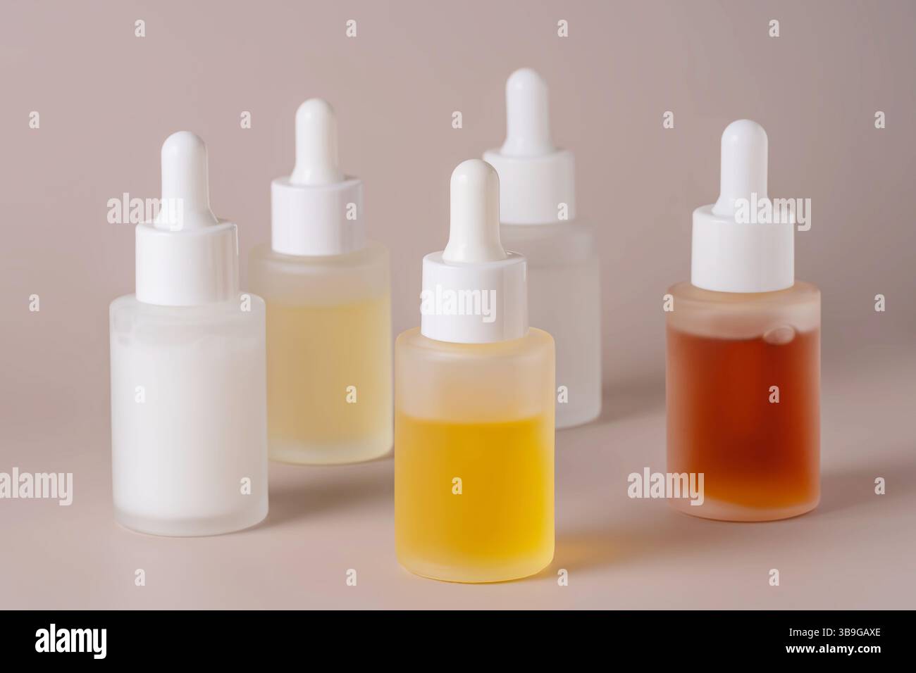 Dieses Bild zeigt eine Sammlung von fünf durchscheinenden Tropfflaschen mit verschiedenfarbigen Flüssigkeiten auf weichem beigem Hintergrund, ideal für Wellness und Wellness Stockfoto