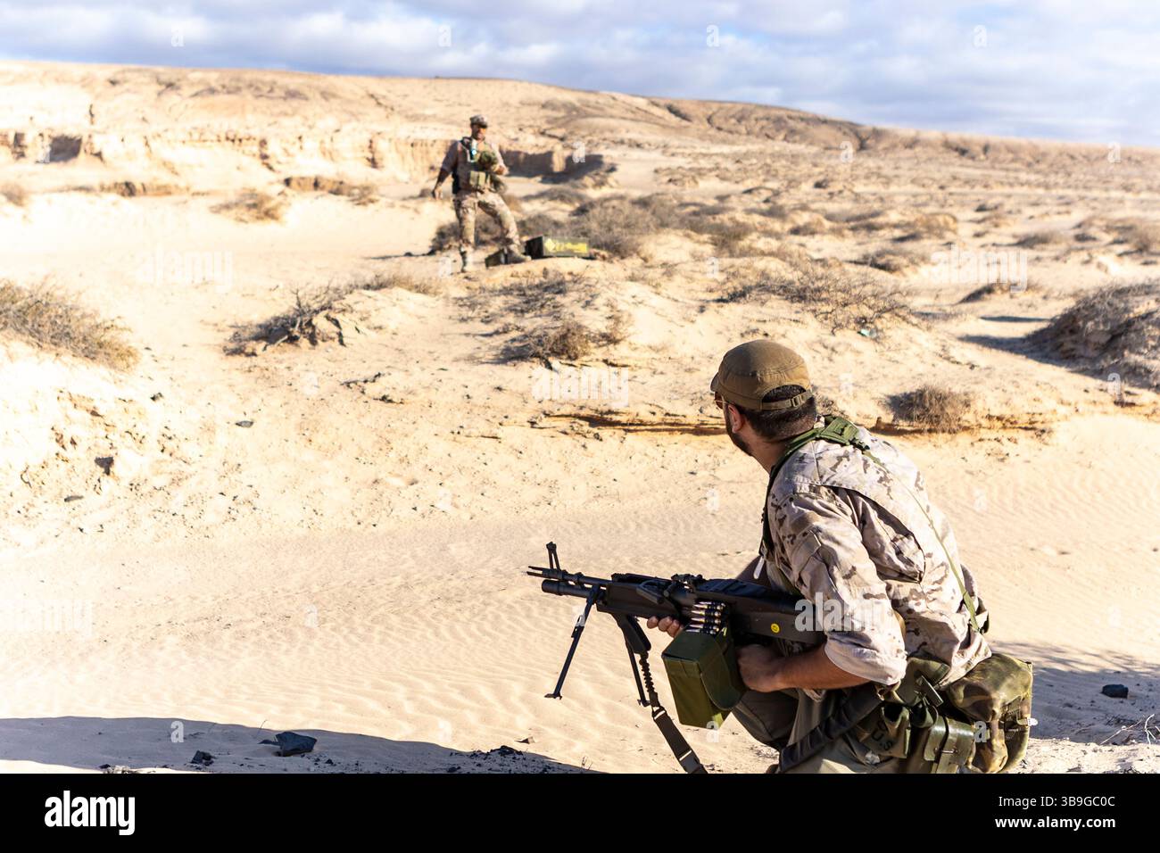 Zwei Soldaten in Tarnausrüstung führen Trainingsübungen in einer Wüstenumgebung durch. Ein Soldat hält ein Gewehr und demonstriert die militärische Bereitschaft A Stockfoto