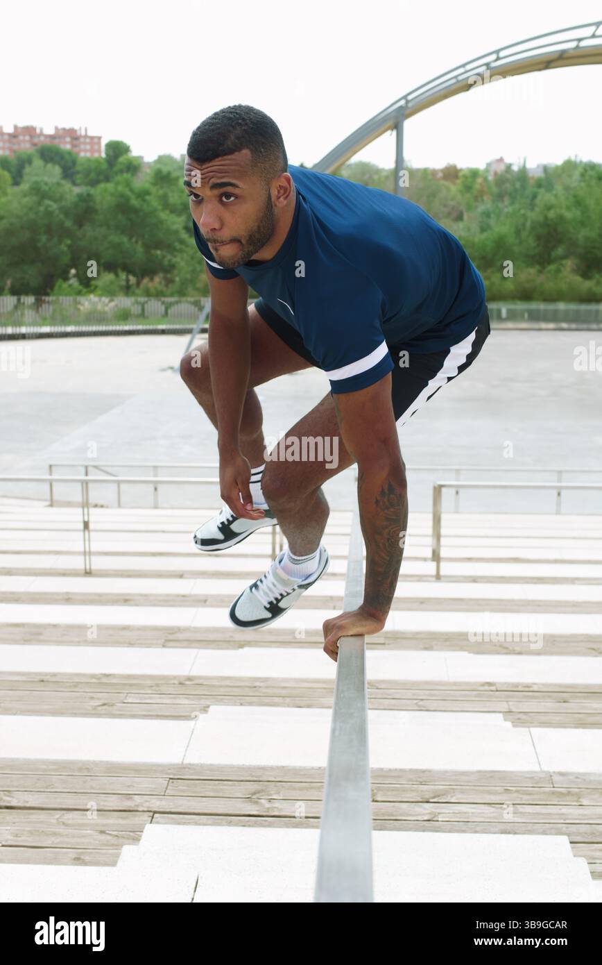 Ein schwarzer männlicher Athlet, der auf einer Außentreppe energisch Parkour übt und Agilität und Entschlossenheit in einer städtischen Umgebung demonstriert. Perfekt für Stockfoto