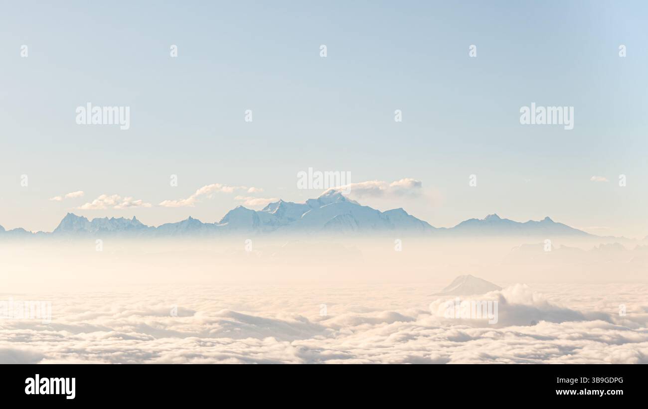 Ein ruhiges Luftbild, das die majestätischen Alpen zeigt, die durch eine dichte Wolkendecke unter einem klaren Himmel hindurchblicken und die ruhige Schönheit hervorheben Stockfoto