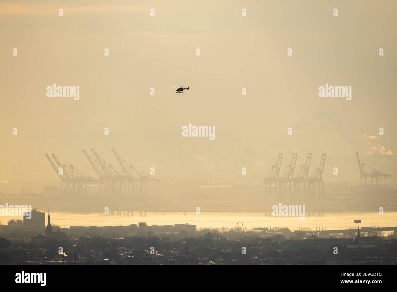 Ein nebeliger Blick auf den Hafen von New York mit einem Hubschrauber, der über einer Silhouette von Schiffskränen und entfernten Nebelküsten schwebt. Stockfoto