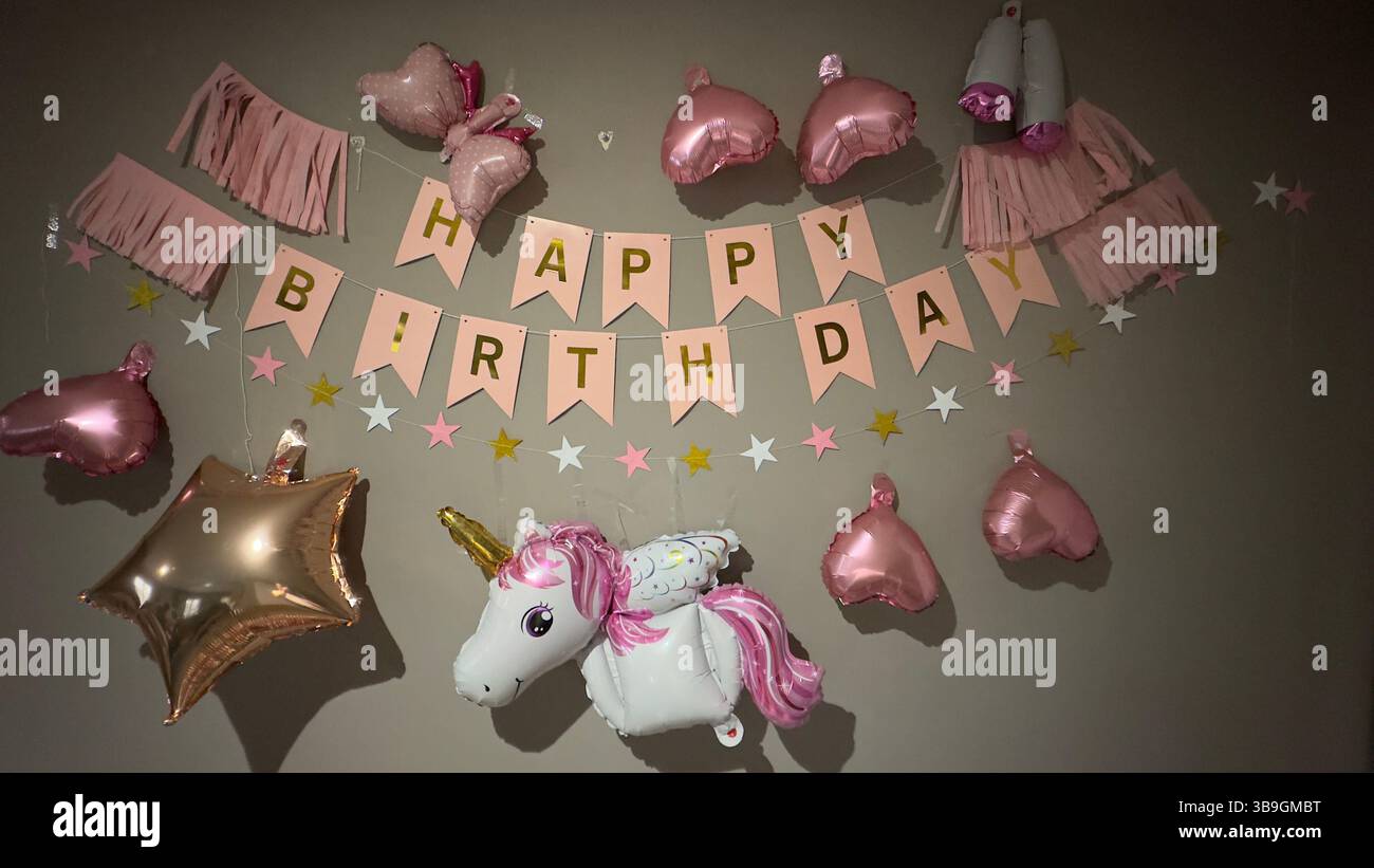Geburtstagsdekoration mit einem „Happy Birthday“-Banner, Ballons und einer Sterngirlande auf einer grauen Wand. Stockfoto