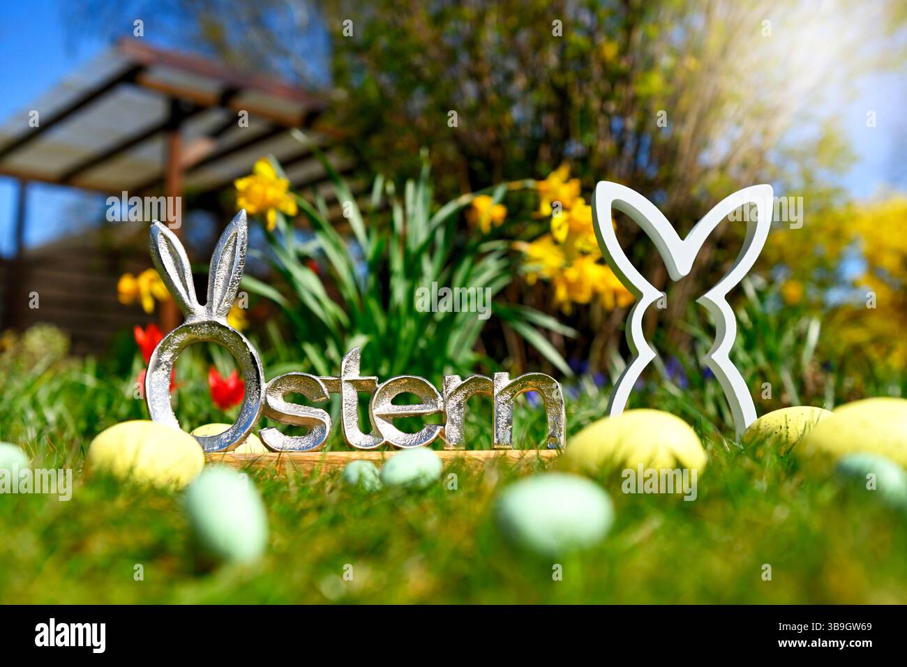 Osterhasenfigur mit Ostereiern vor Frühlingsblumen und Osterbuchstaben Stockfoto