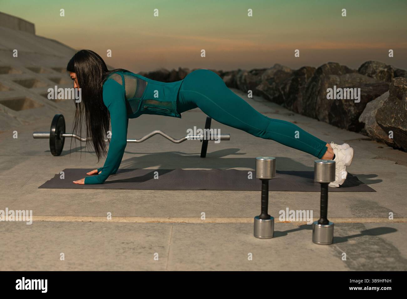 Die Person nimmt an einer Plank-Übung auf einer Trainingsmatte Teil, die sich in felsigem Gelände befindet, während die Sonne untergeht und einen konzentrierten und entschlossenen Ausdruck zeigt. Stockfoto