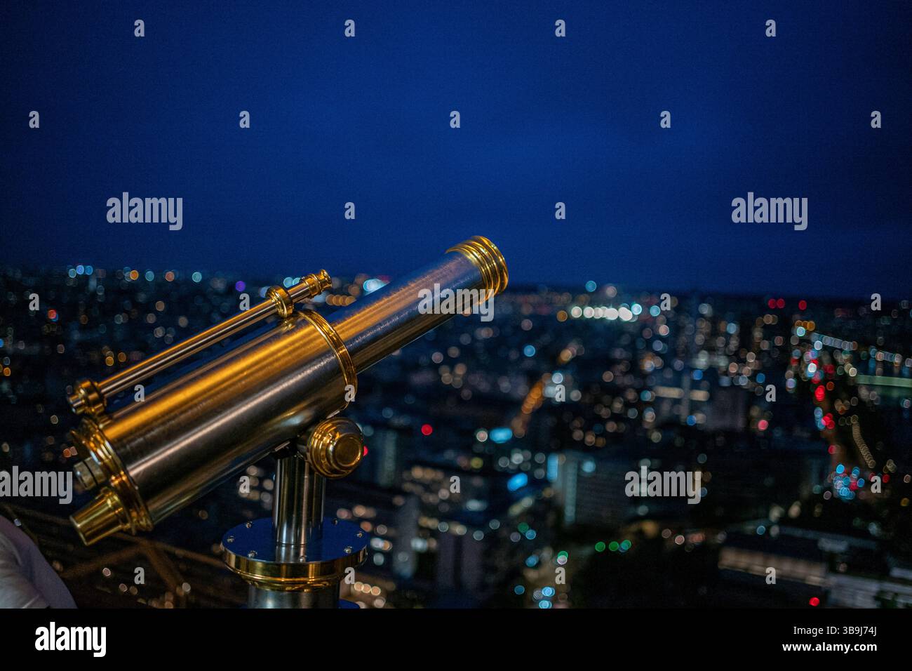 Ein Chrom-Teleskop auf dem oberen Deck des legendären Eiffelturms von Paris, das die wunderschöne Stadt bei Nacht überblickt, Paris, Frankreich Stockfoto