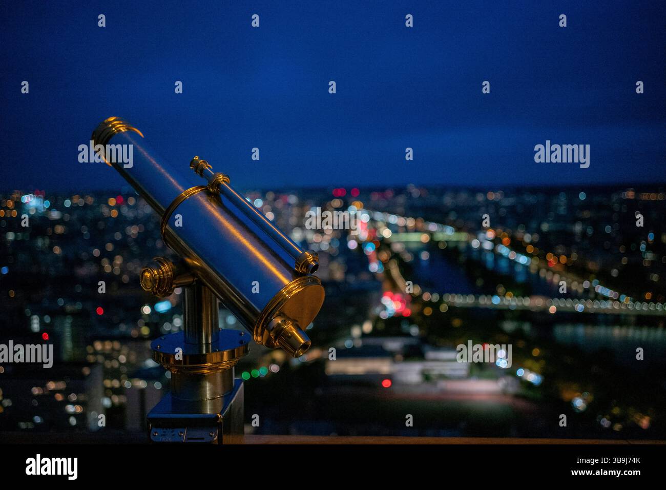 Ein Chrom-Teleskop auf dem oberen Deck des legendären Eiffelturms von Paris, das die wunderschöne Stadt bei Nacht überblickt, Paris, Frankreich Stockfoto