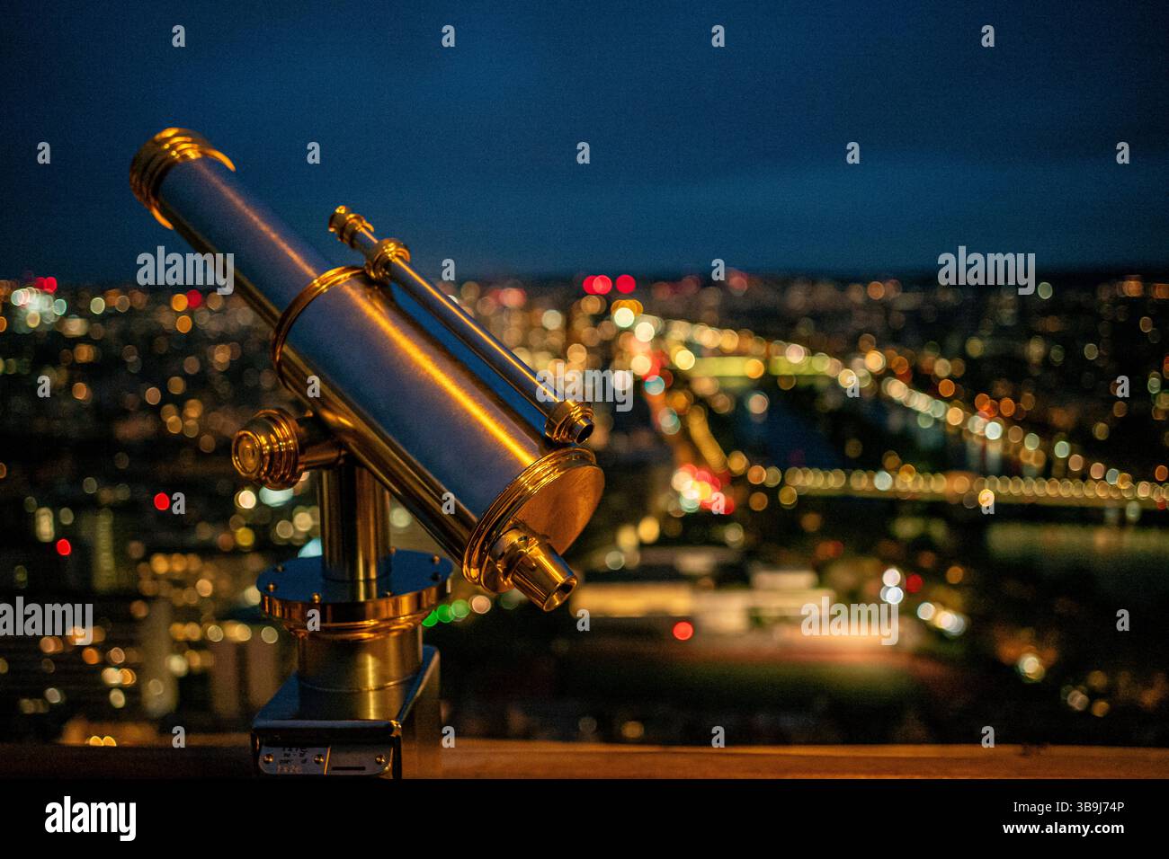 Ein Chrom-Teleskop auf dem oberen Deck des legendären Eiffelturms von Paris, das die wunderschöne Stadt bei Nacht überblickt, Paris, Frankreich Stockfoto