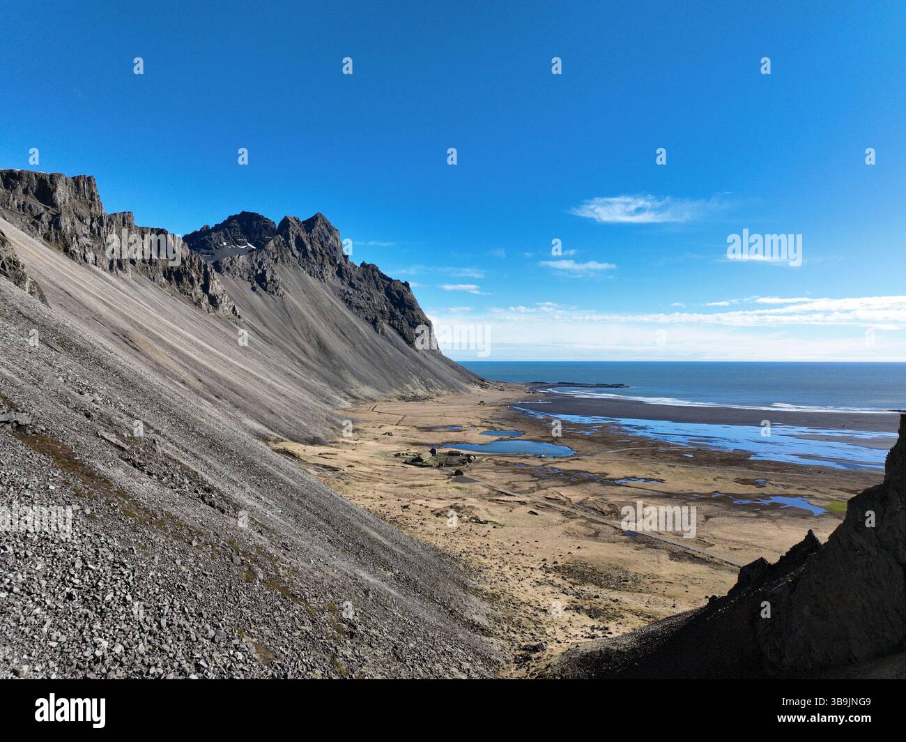 Majestätische, zerklüftete Gipfel des Vestrahorn Mountain dominieren eine krasse Küstenlandschaft mit Wattflächen und dem riesigen Atlantischen Ozean unter klarem Himmel Stockfoto