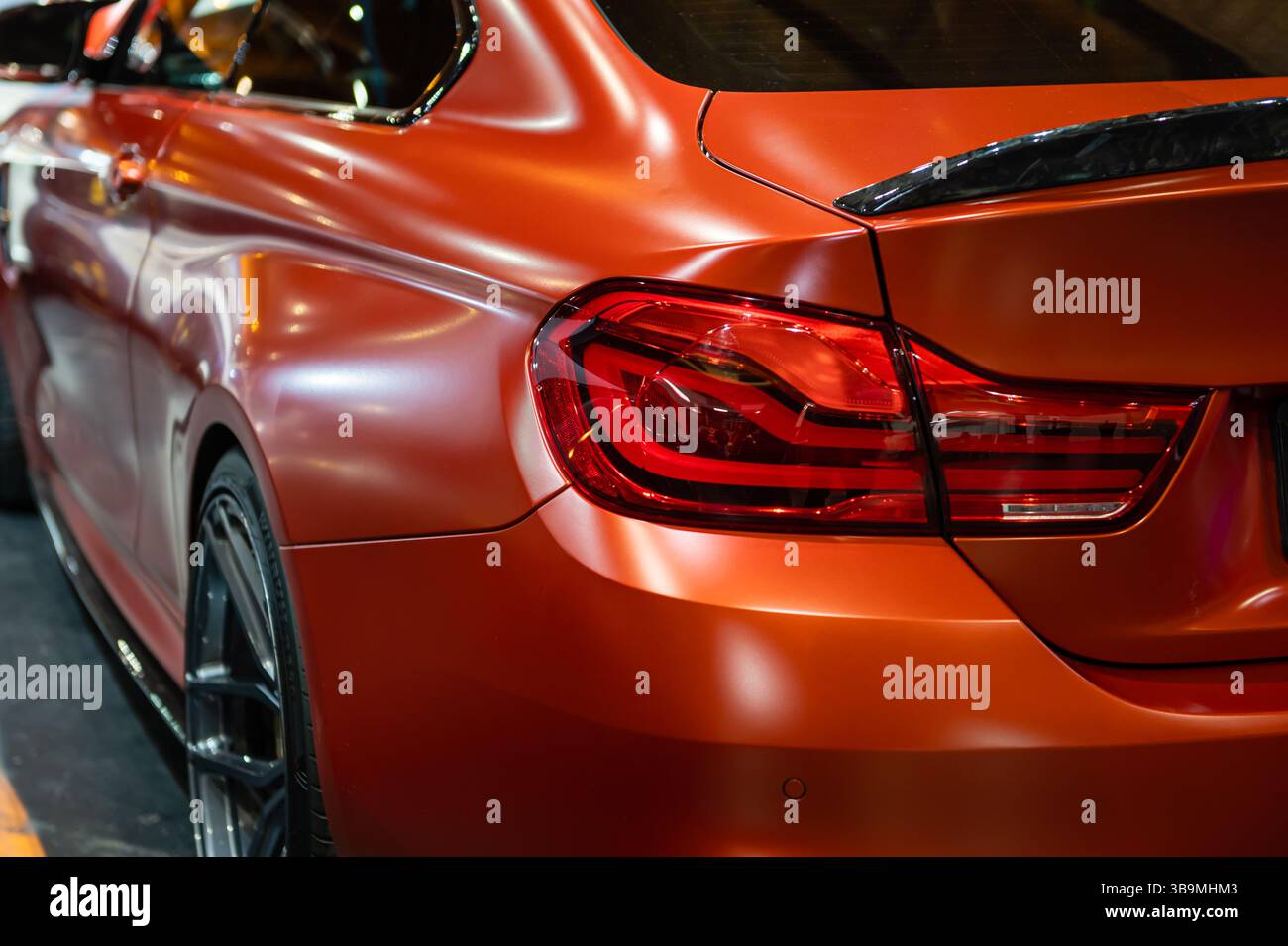 Riga, Lettland, 29. April 2022: Besucher bewundern die atemberaubenden Kurven und Details eines leuchtenden orangen Fahrzeugs auf der Ausstellung. Stockfoto