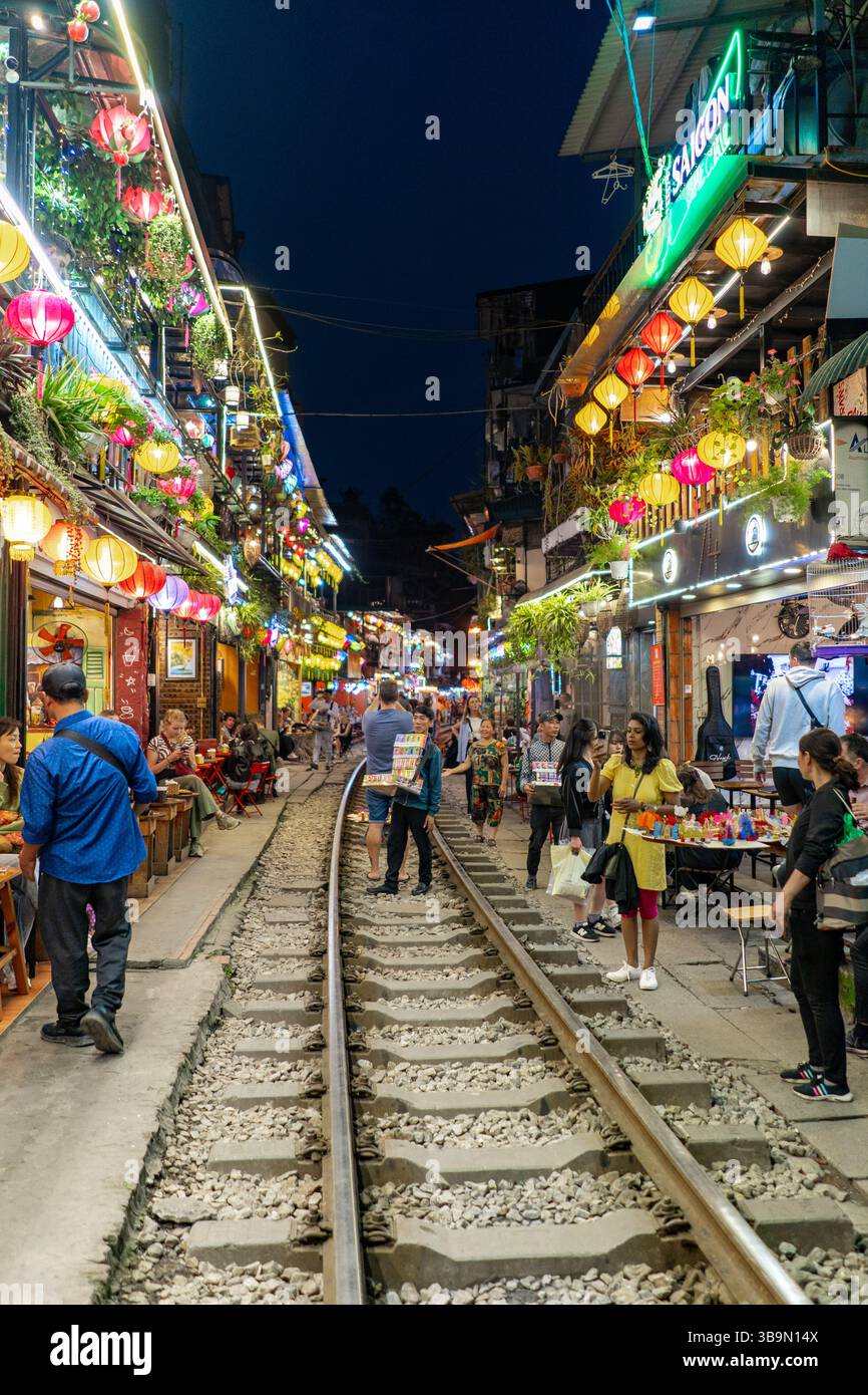 Die Menschen schlendern nachts auf den Spuren der berühmten Hanoi-Bahnstraße, die von farbenfrohen Laternen und Lichtern beleuchtet wird. Stockfoto