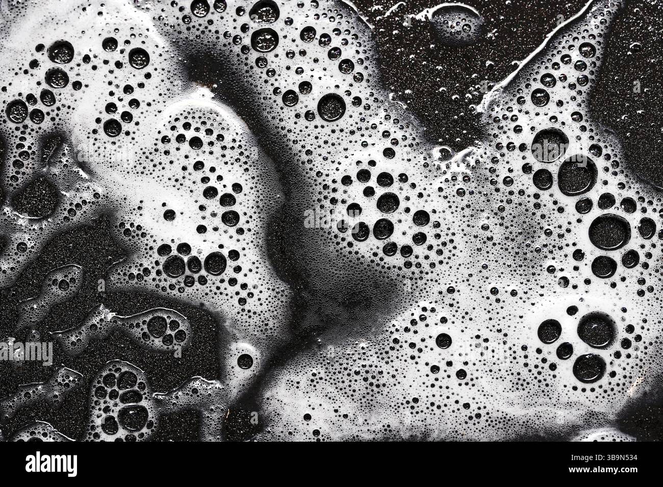 Abstrakte Textur aus Seifenschaum. Weiße Blasen auf schwarzer Oberfläche. Hintergrundmakro wird bereinigt. Waschmittelrückstände. Waschmittelmuster, Draufsicht. Stockfoto