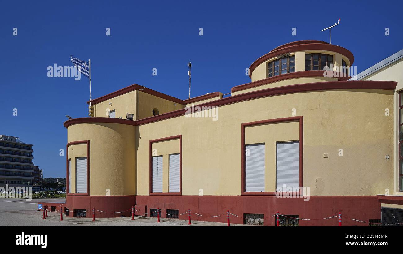 Altes Aquarium an der Nordspitze von Rhodos, gelbes Gebäude mit runden Fenstern und griechischer Flagge vor einem klaren blauen Himmel, Hafengebiet, Rhodos-Stadt, Rho Stockfoto