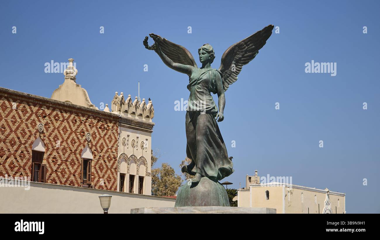 Statue eines Engels mit Flügeln vor einer dekorativen Fassade, Bronzestatue, Platia Antinavarchou Perikli Ioannidi, Hafengebiet, Rhodos-Stadt, Rhode Stockfoto