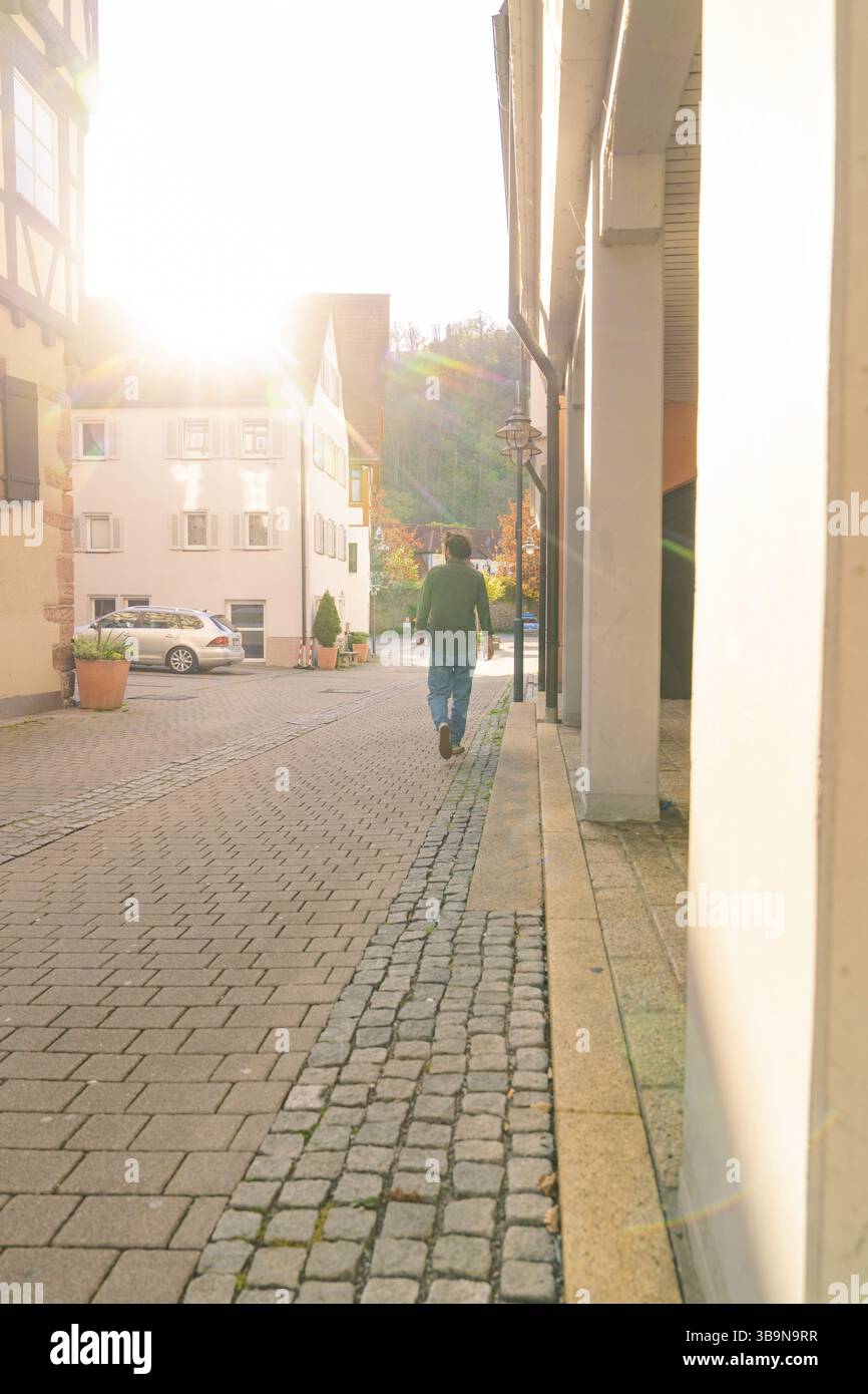 Person, die im Sonnenlicht durch eine ruhige Kopfsteinpflasterstraße mit Gebäuden läuft, Nagold, Schwarzwald, Deutschland, Europa Stockfoto