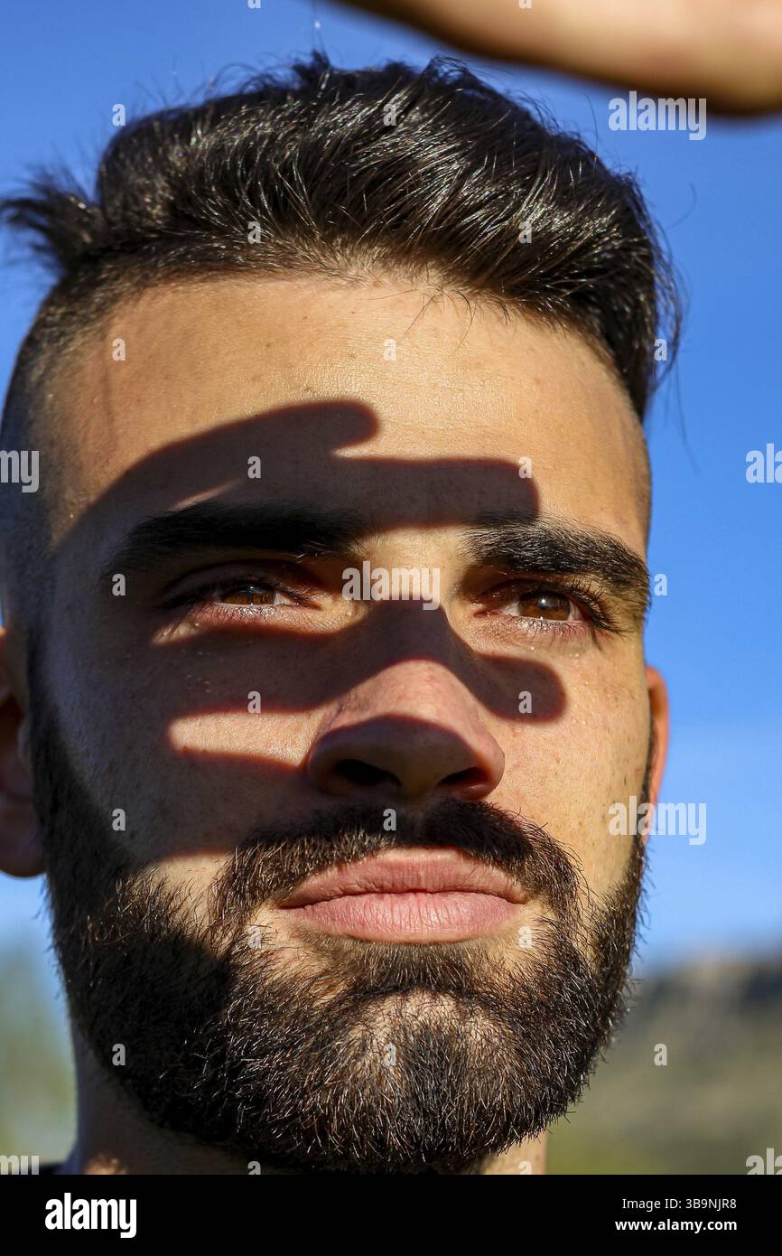 Vertikale Nahaufnahme eines lächelnden Bart-Mannes, der während des Sonnenuntergangs in einem gelben Feld die Sonne mit seiner Hand bedeckt Stockfoto