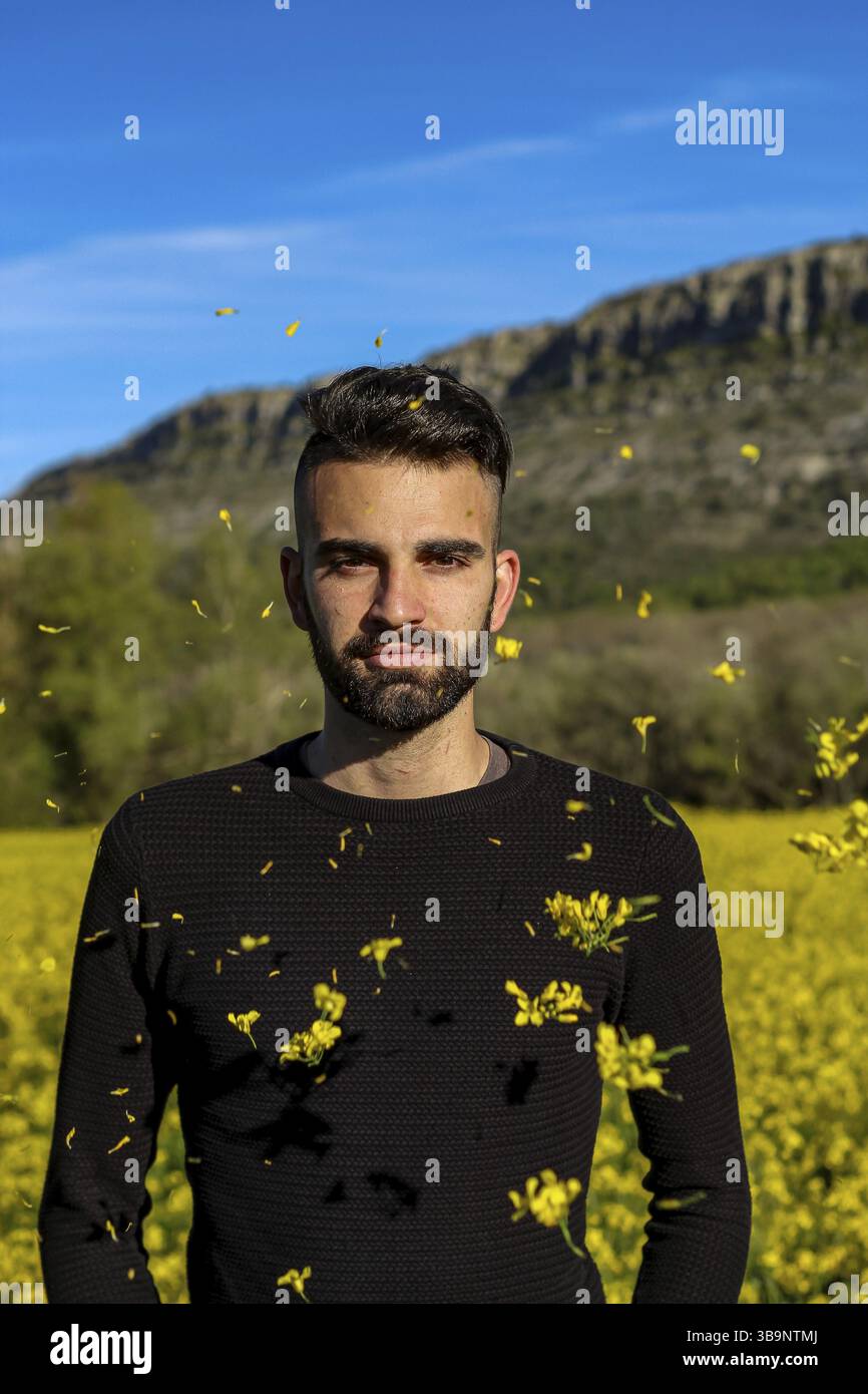 Vertikales Porträt eines lächelnden jungen Mannes in einem gelben Blumenfeld im Frühlingssommer an einem sonnigen Tag Stockfoto