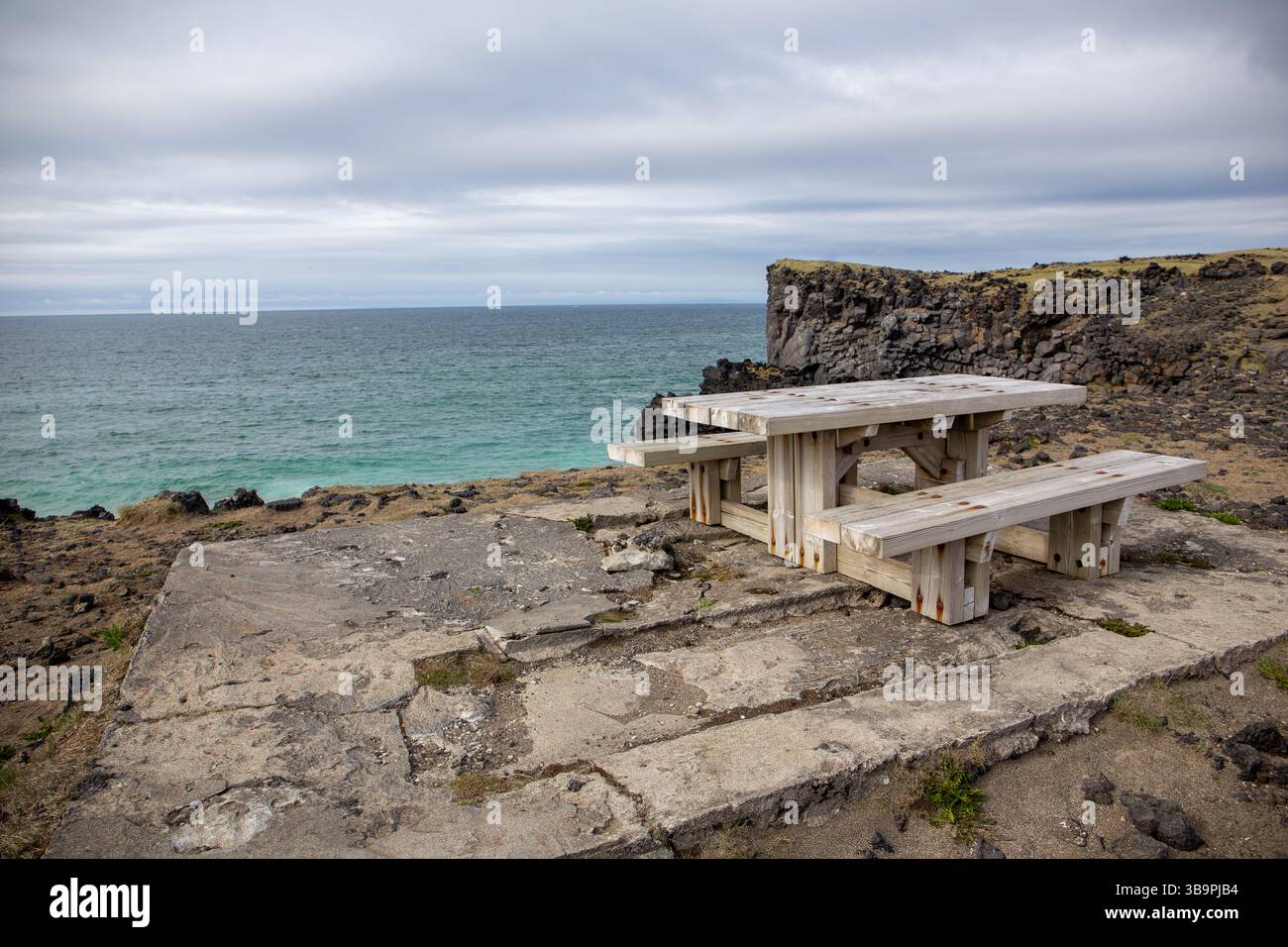 Picknickbereich mit Holztisch und Bank am Skardsvik Beach auf der Halbinsel Snaefellsnes in Island mit Meerblick und vulkanischen Klippen. Stockfoto