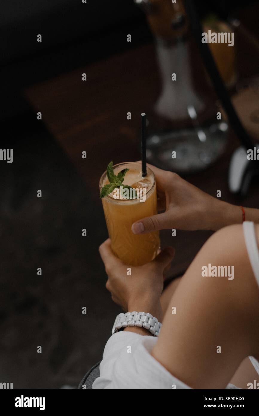 Eine Frau, die ein erfrischendes Orangengetränk mit Pfefferminze hält. Entspannte Atmosphäre und ungezwungene Indoor-Szene. Stockfoto Eine Frau, die ein erfrischendes Orangengetränk mit Pfefferminze hält. Entspannte Atmosphäre und ungezwungene Indoor-Szene. Stockfoto