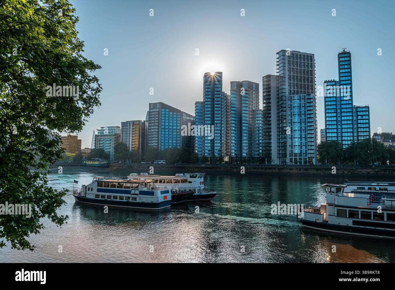 Das Sonnenlicht am frühen Morgen beleuchtet moderne Hochhäuser entlang der Themse, mit Flussbooten, die friedlich durch das ruhige Wasser des Zentrums gleiten Stockfoto