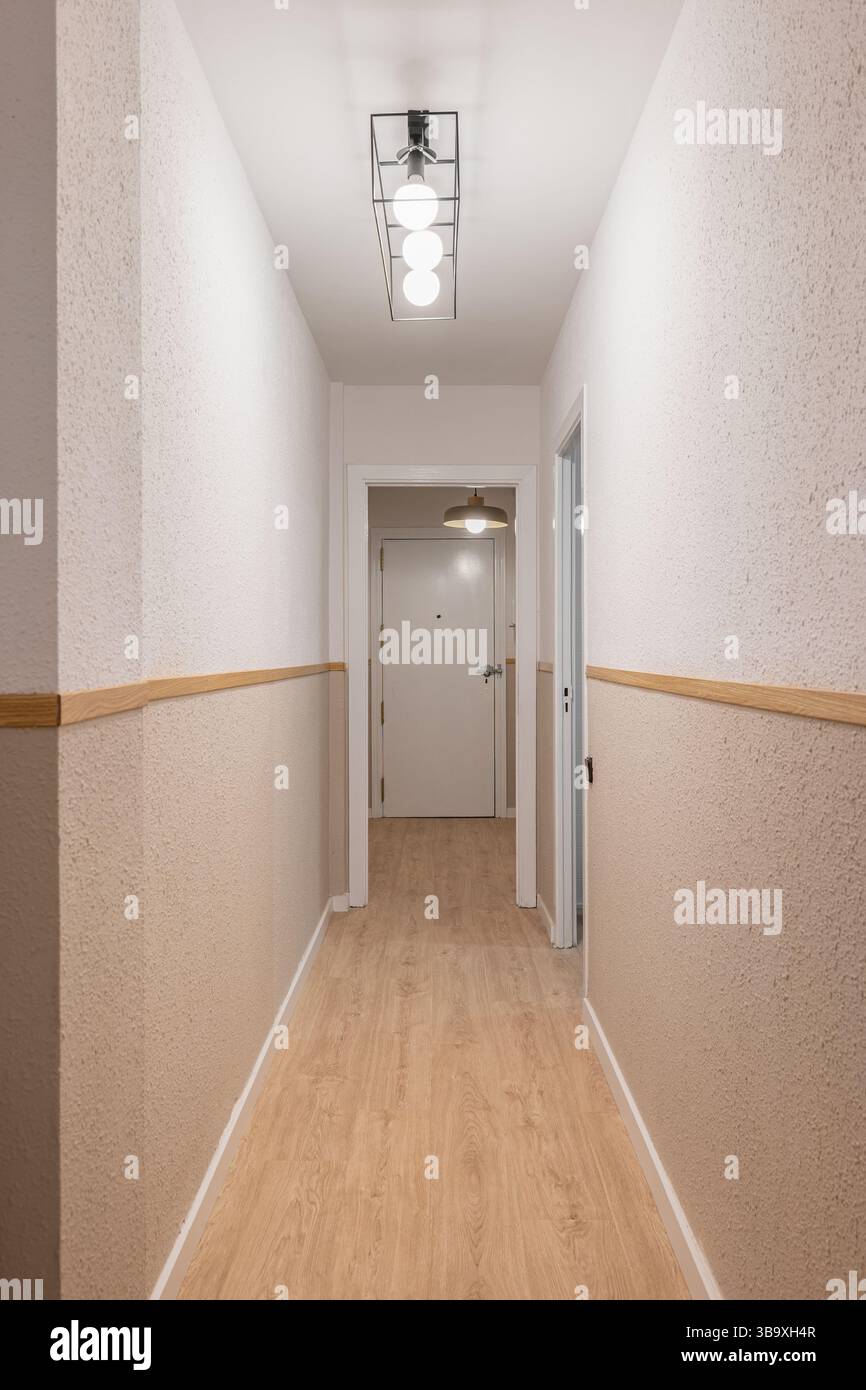Innenkorridor mit Holzfußboden, weißen Türen, strukturierten beigefarbenen Wänden und Deckenleuchten in linearer Anordnung Stockfoto