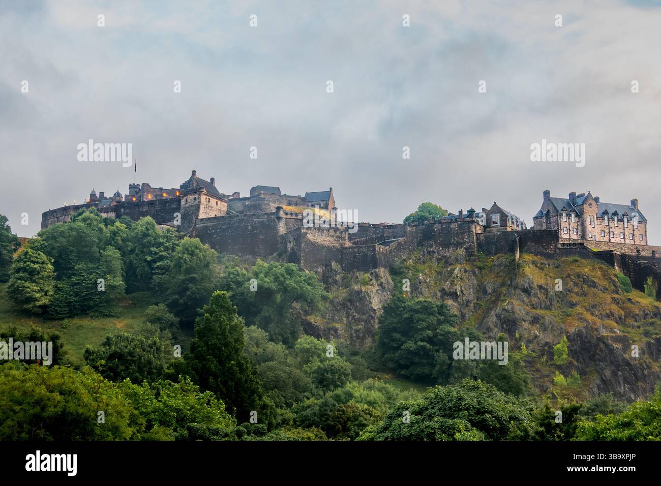 Edinburgh Castle in Schottland auf dem Castle Rock Mountain, umgeben von üppigen grünen Bäumen an einem bewölkten Sommerabend aus dem Norden Stockfoto
