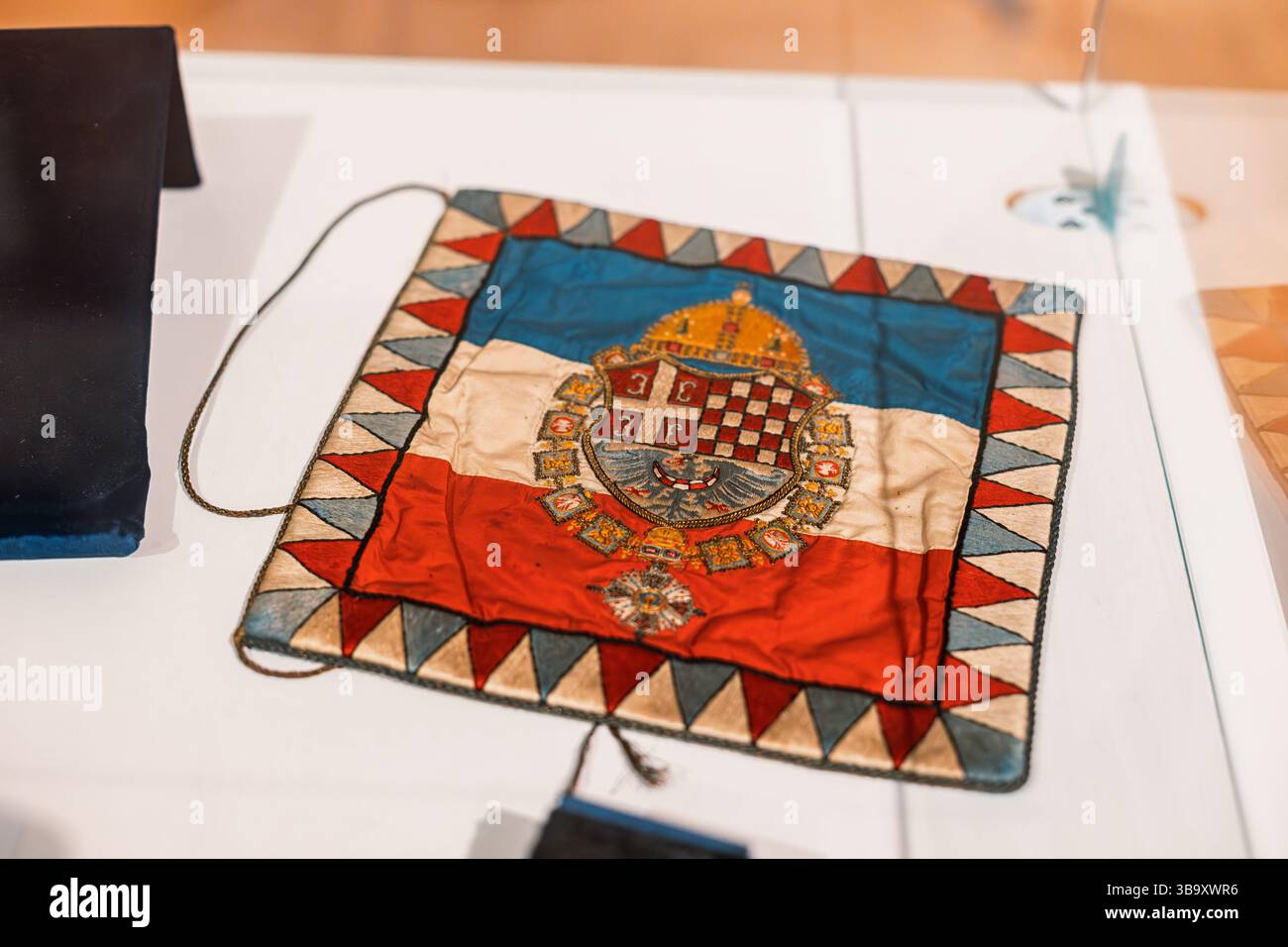 15. Februar 2025, Belgrad, Serbien: Flagge des Königreichs Kroatien Slawonien mit Wappen auf weißer Oberfläche in Museumsausstellung Stockfoto