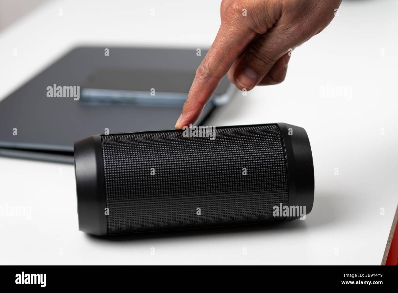 Nahaufnahme einer männlichen Hand, die zu Hause einen tragbaren roten Lautsprecher anschließt.Geschäftsmann genießt seine Lieblingsmusik, während er durch sein Smartphone scrollt.Techno Stockfoto