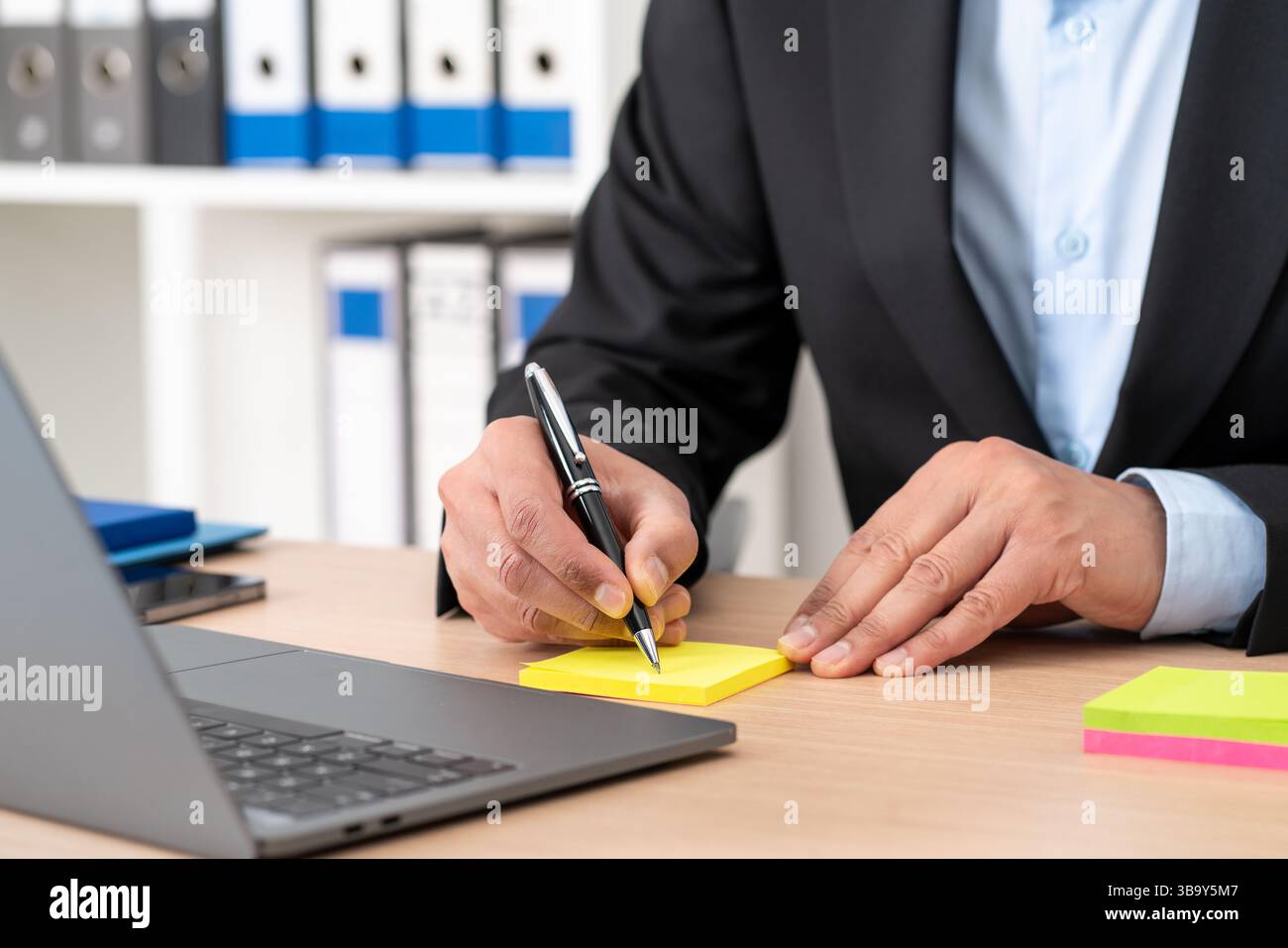 Nahaufnahme eines Geschäftsmanns, der im Büro auf Postnotiz schreibt Stockfoto