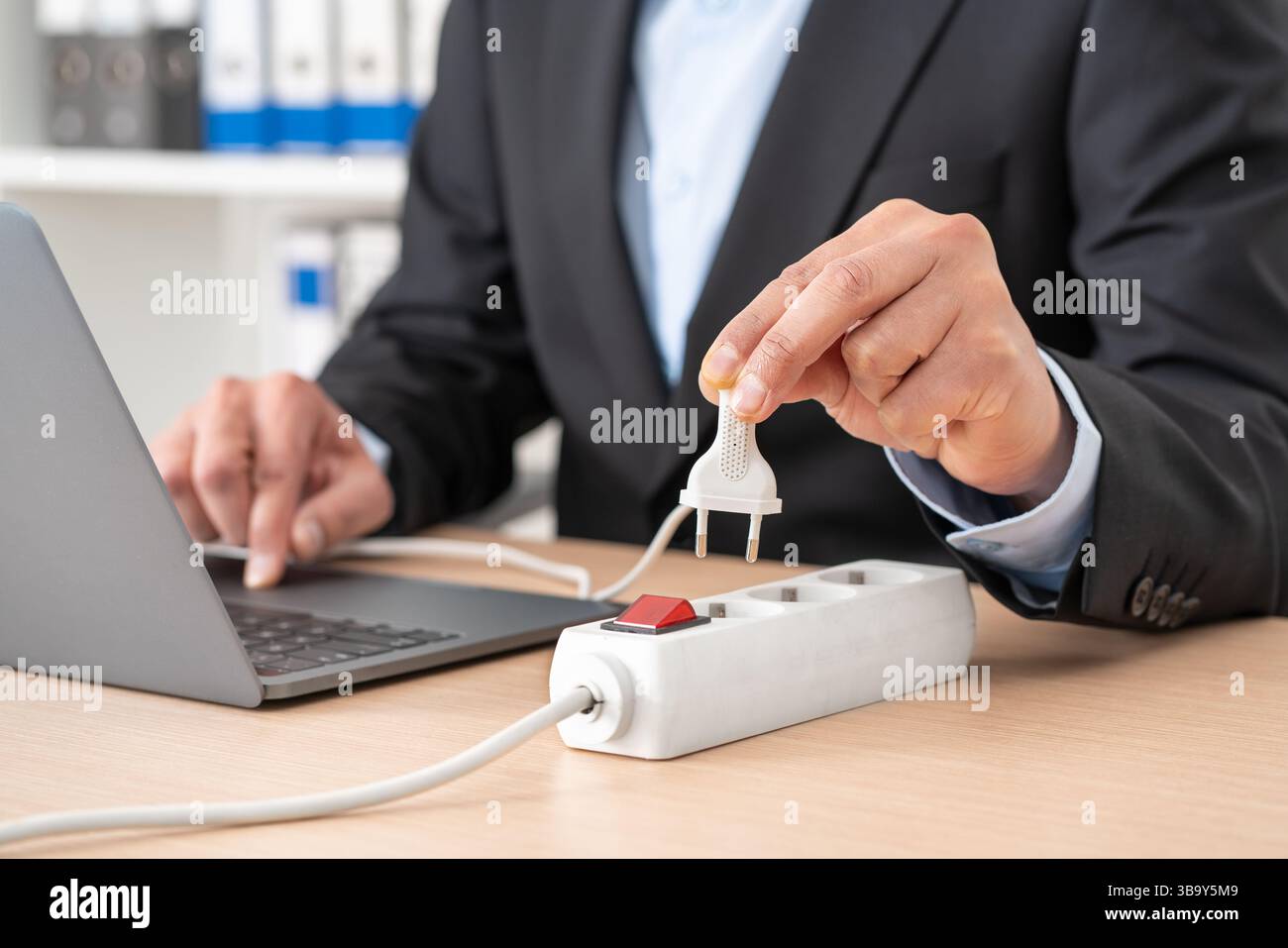 Nahaufnahme eines Mannes, der den Stecker an einer Steckdosenleiste mit einem Laptop auf einem Schreibtisch im Büro steckte Stockfoto