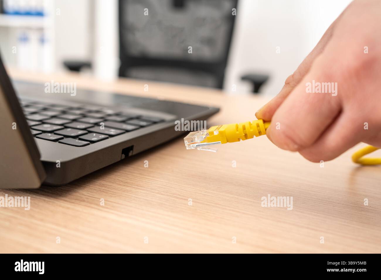 Nahaufnahme von Frauenhänden, die ein ethernet-Kabel an einen Laptop auf einem Desktop anschließen Stockfoto