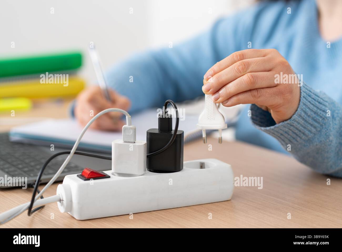 Weibliche Schülerin, die den Stecker an einer Steckdosenleiste mit dem Laptop auf dem Schreibtisch zu Hause steckte Stockfoto