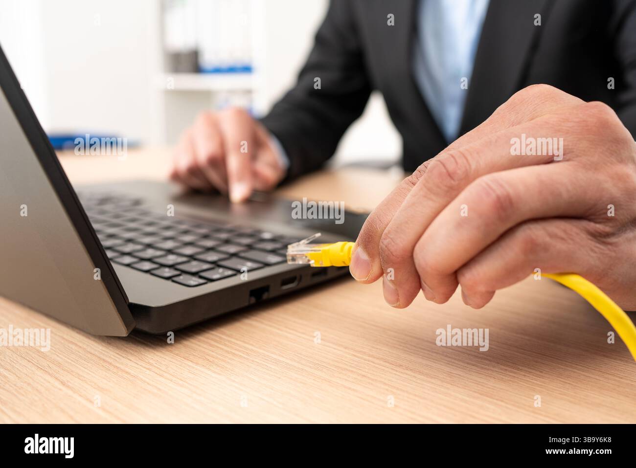 Nahaufnahme eines Geschäftsmanns, der ein ethernet-Kabel an einen Laptop an einem Desktop-PC angeschlossen hat Stockfoto