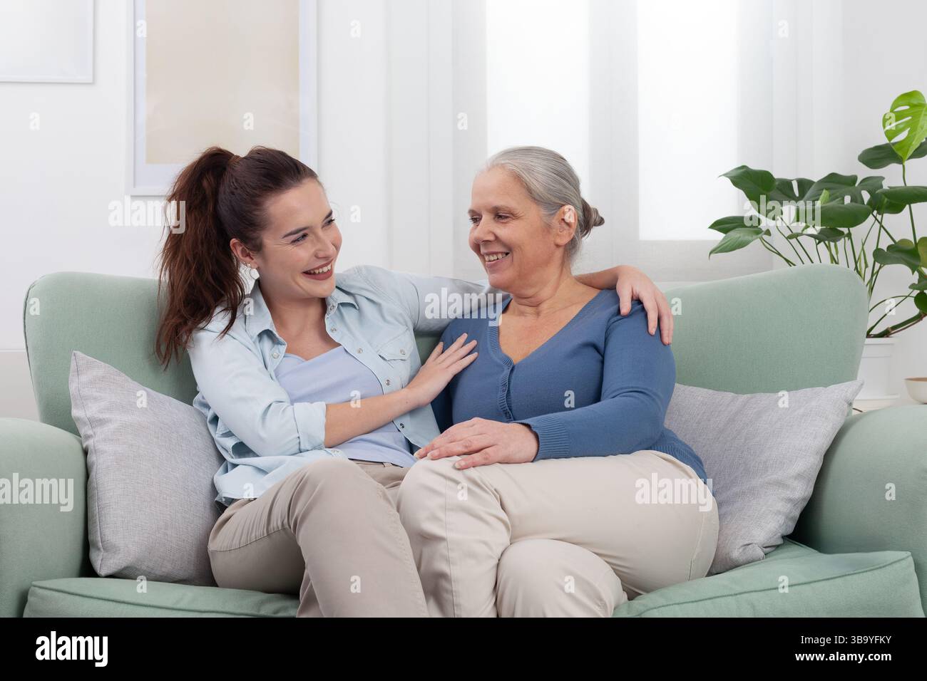 Enkelin umarmt ihre lächelnde Großmutter mit Liebe und Freude. Ein herzlicher und glücklicher Familienmoment zu Hause, der Zuneigung, Verbundenheit und generationenfreundliches Vergnügen zeigt Stockfoto