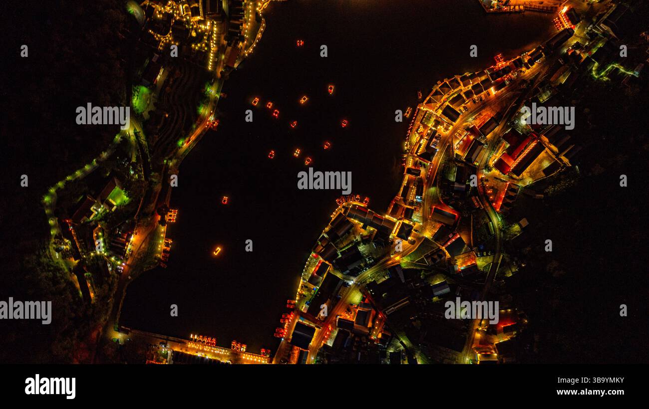 Ein atemberaubender Blick bei Nacht auf das Bergdorf Baan Rak Thai, das mit warmen goldenen Lichtern geschmückt ist und sich wunderbar auf dem ruhigen Wasser spiegelt. Der dunkle Himmel W Stockfoto