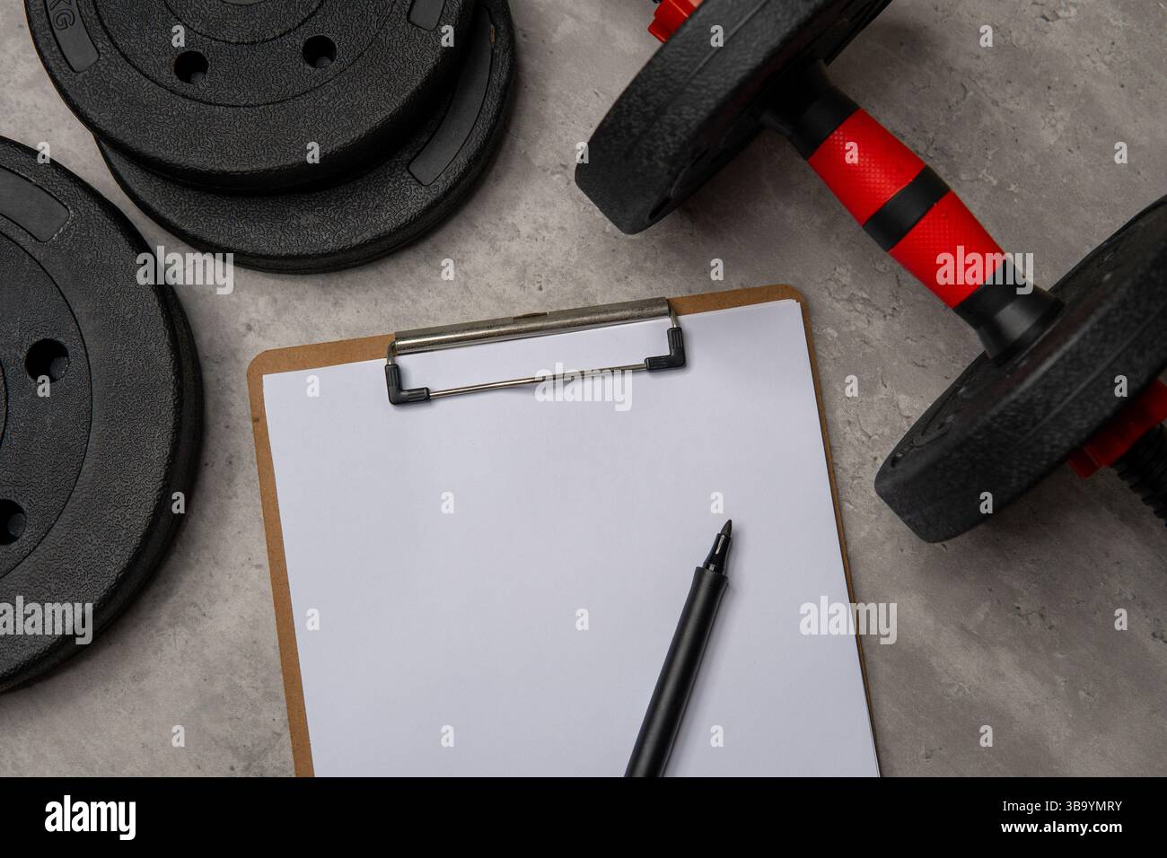 Ein leeres weißes Blatt Papier auf einer Zwischenablage, Hantelplatten und Hantel. Fitnessplanung, Trainingsverfolgung oder Zielfindungskonzept. Stockfoto