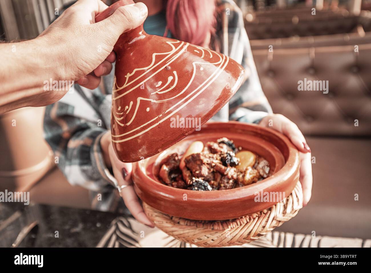 Nahaufnahme einer traditionellen marokkanischen Tajine mit Lamm, getrockneten Früchten und Gewürzen, die von einem Kellner in einem Restaurant entdeckt werden Stockfoto