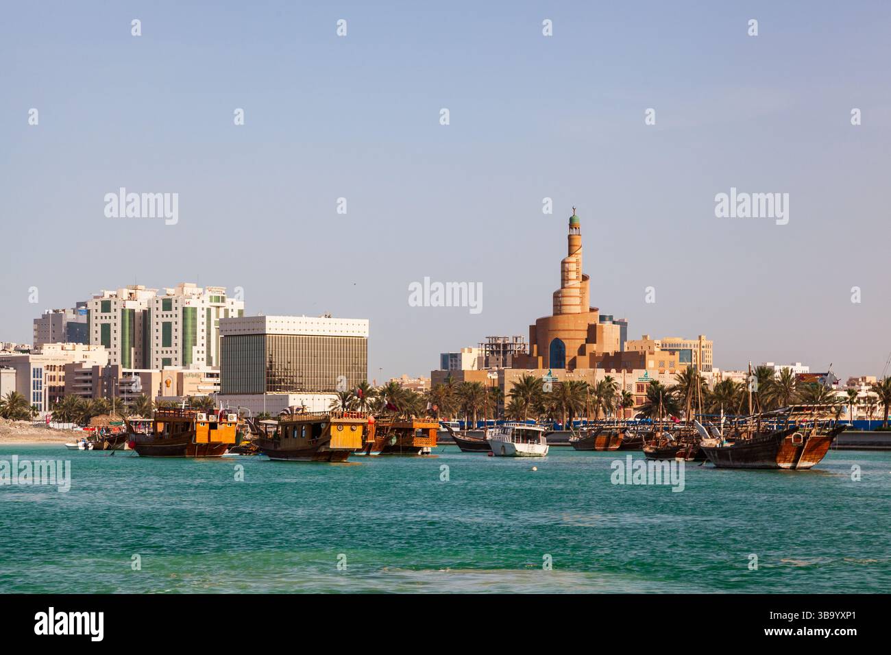 Blick bei Sonnenuntergang auf traditionelle Dhow Holzboote im Corniche Hafen und MIA Park am Al Souq Touristenmarkt und Moschee, der Hauptstadt von Katar. Stockfoto