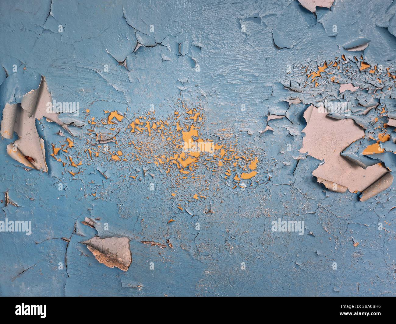 Betonwand in Nahaufnahme mit abblätternder blauer Farbe, die Flecken von gelber Emaille darunter freigibt. Raue Textur Hintergrund Alterung, Verwitterung und Verschlechterung - Smartphone-aufgenommenes Stockfoto