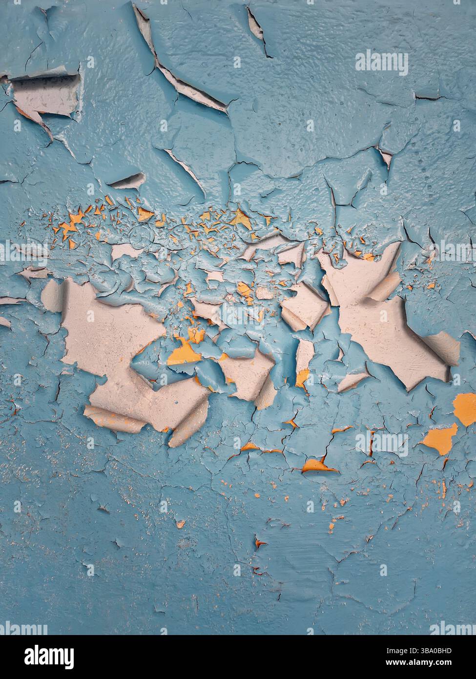 Betonwand in Nahaufnahme mit abblätternder blauer Farbe, die Flecken von gelber Emaille darunter freigibt. Raue Textur Hintergrund Alterung, Verwitterung und Verschlechterung - Smartphone-aufgenommenes Stockfoto
