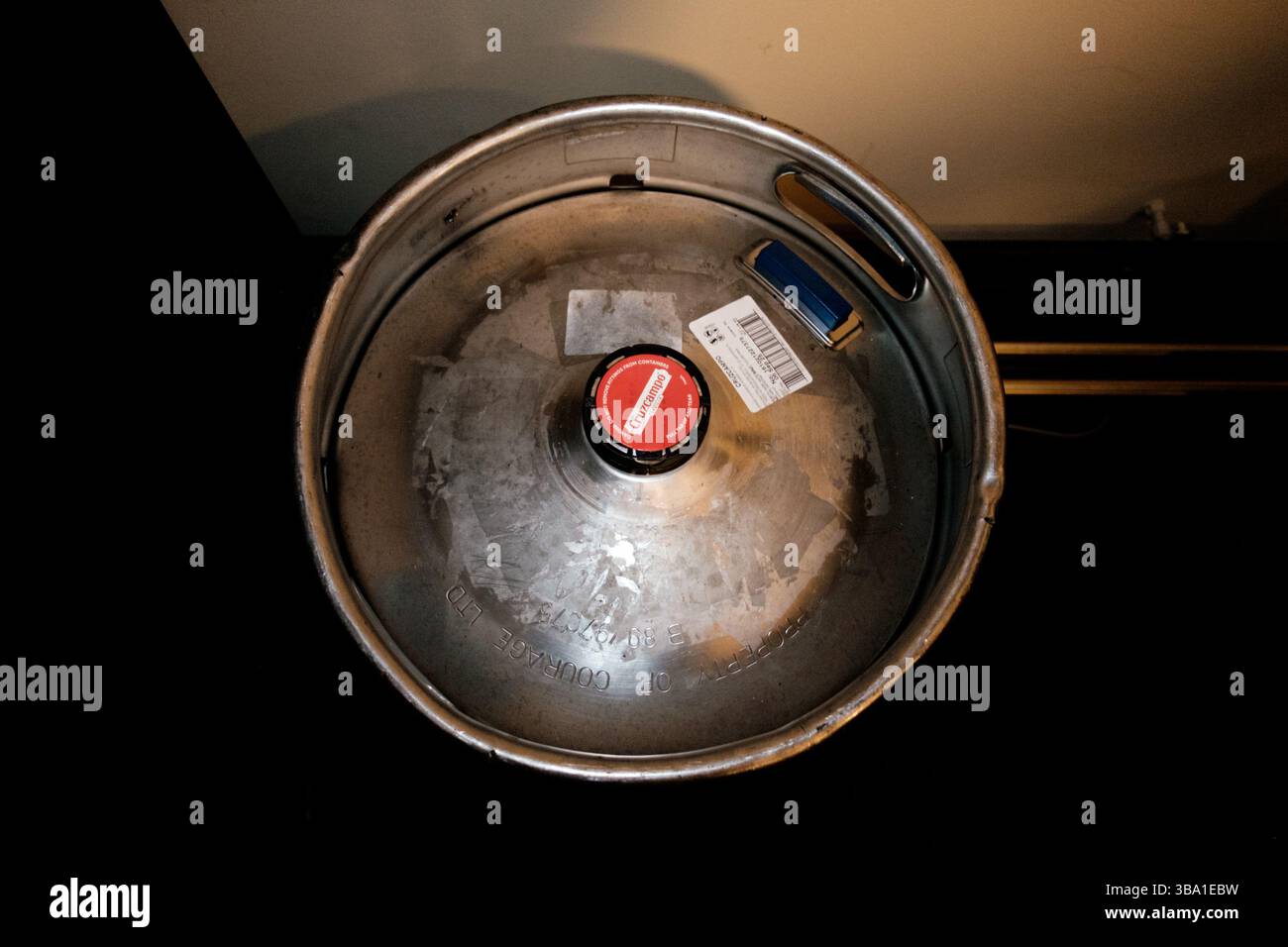 Newcastle UK: 22.03.2025: Ein Metallfass mit einem markanten Cruzcampo-Brauereilabel liegt auf einer dunklen Oberfläche und zeigt seine runde Form und die rote Oberseite Stockfoto