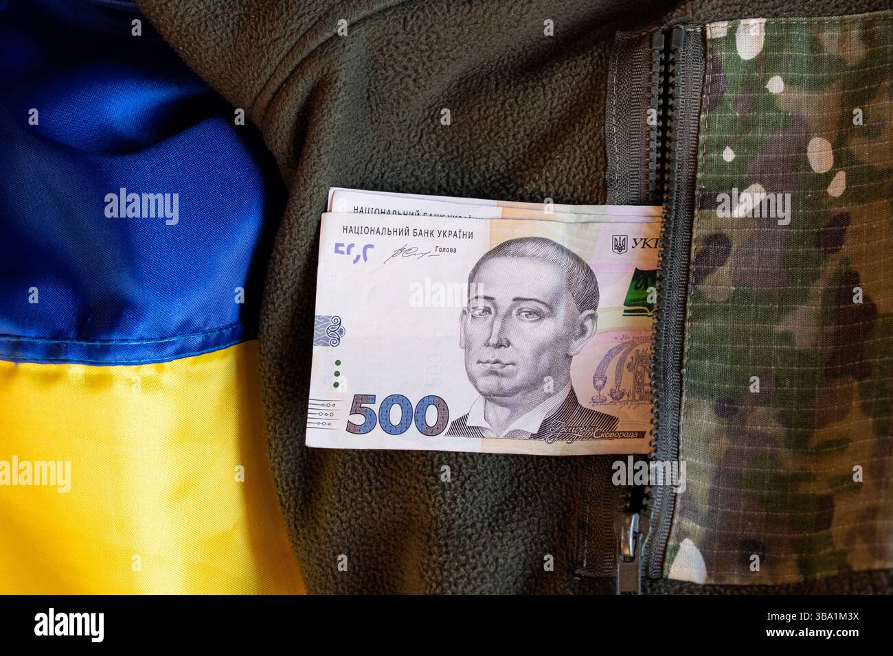 500 Hrywnja liegen in einer Tasche in Militäruniform auf der Flagge der Ukraine, Gehälter und Zahlungen für das Militär Stockfoto