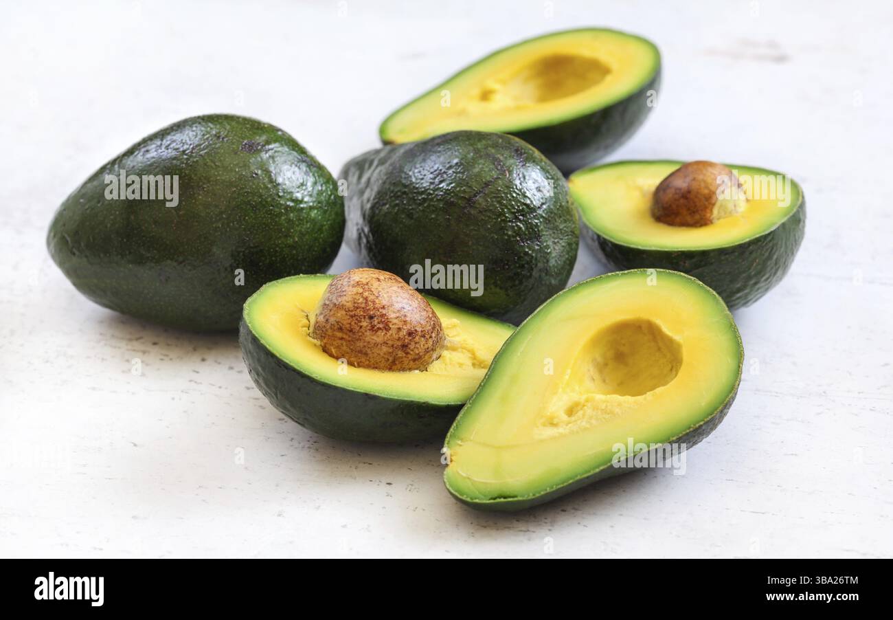 Avocados, ganz und halbiert - Samen sichtbar, auf weißem Arbeitsbrett, Liptovsky Hradok, Slowakei, Europa Stockfoto